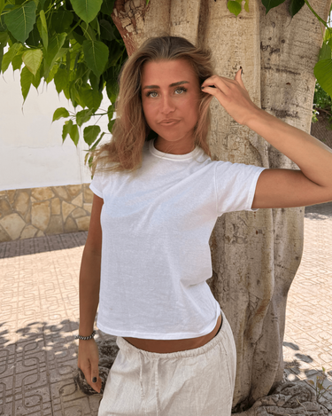 Model i hvid, tætsiddende Fruit babytee i bomuld, stående ved et træ
